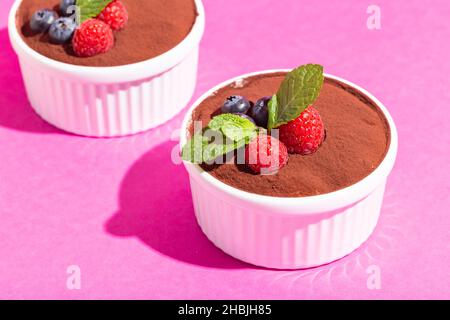 Perfekter hausgemachter Tiramisu-Kuchen mit frischer Minze. Tiramisu Teil in weißer Platte auf rosa Hintergrund harte Schatten. Stockfoto