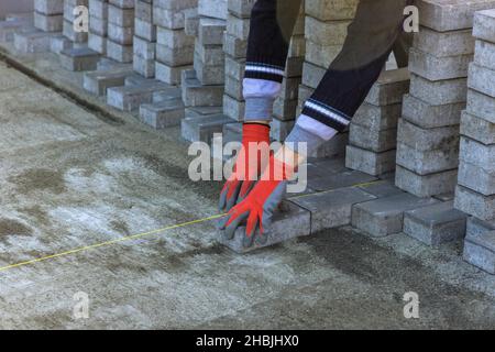 Der Meister in Handschuhen legt Pflastersteine in Schichten Gehweg Pflaster durch professionelle Fertiger Arbeiter. Stockfoto