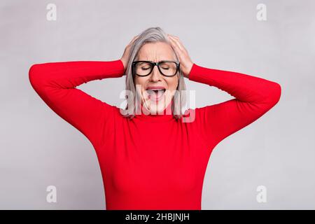 Foto von unglücklichen alten traurigen Frau halten Hände Kopf tragen Brille Kopfschmerz isoliert auf grauem Hintergrund Stockfoto