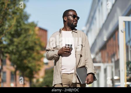 Porträt eines schwarzen Mannes, der im Freien eine Sonnenbrille trägt, während er in der Stadt zur Kamera geht und den Raum kopiert Stockfoto