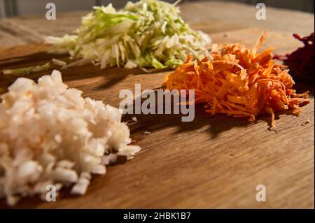 Nahaufnahme von gehackten Zutaten für ein traditionelles ukrainisches Suppenborscht. Gehackte und geriebene rohe frische Gemüse -Rüben, Karotten Zwiebeln und Kohl auf Stockfoto