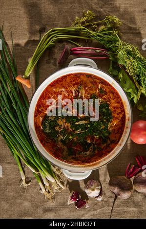 Flach liegend. Draufsicht auf ukrainische traditionelle Suppe - Borscht - mit frischem Gemüse, Kohl, Tomaten, Rote Beete, Karotten und Grennerien auf Leinentisch Stockfoto