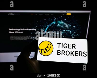 Person, die das Smartphone mit dem Logo der Firma UP Fintech Holding Limited (Tiger Brokers) auf dem Bildschirm vor der Website hält. Konzentrieren Sie sich auf die Telefonanzeige. Stockfoto