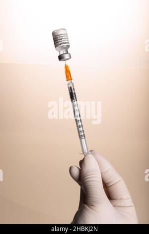 Turin, Italien - 18. Dezember 2021: Pfizer-BioNTech COVID-19-Impfstoff Comirnaty-Fläschchen, Hand mit Latexhandschuh und Spritze, die die Impfdosis aus dem Fläschchen zieht Stockfoto