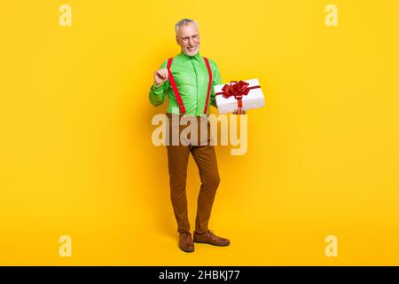 In voller Länge Foto von im Alter gut aussehend Mann glücklich positive Lächeln flirty halten Geschenk Feier isoliert über gelbe Farbe Hintergrund Stockfoto