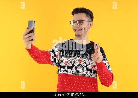 Kerl in Weihnachtspullover mit Telefon auf gelbem Hintergrund Stockfoto