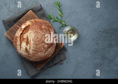 Ein Roggenbrot mit Rosmarin und Olivenöl auf grau-blauem Hintergrund. Draufsicht, Kopierbereich. Stockfoto