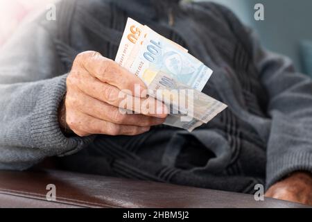 Älterer Mann faltete die Hände mit türkischen Lira-Banknoten.Konzept der Finanzkrise in der Finanzwährung. Stockfoto