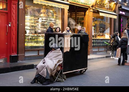 Ein Obdachloser sitzt unter seiner Decke, während er versucht, sich auf den Straßen von London, England und Großbritannien warm zu halten Stockfoto