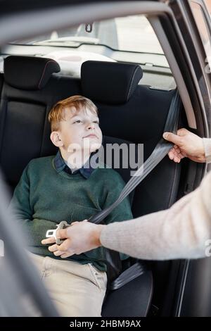 Vertikales Porträt eines blonden Jungen, der sich auf dem Rücksitz des Familienwagens anschnallt und für eine sichere Fahrt bereit ist Stockfoto