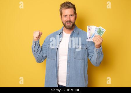 Junger Mann im Denim-Hemd, auf dem Geld auf gelbem Hintergrund steht. Stockfoto