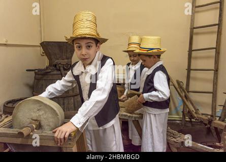 Salaj, Siebenbürgen, Rumänien-13. Mai 2018: Junge Jungen in traditioneller rumänischer Volkstracht, die mit einem alten Steinschleifer und alten Holzwerkzeugen arbeiten Stockfoto