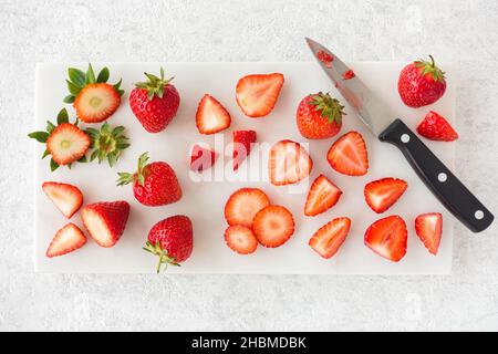 Nahaufnahme von geschnittenen und ganzen Erdbeeren auf weißem Marmor Schneidebrett mit Messer. Draufsicht. Stockfoto
