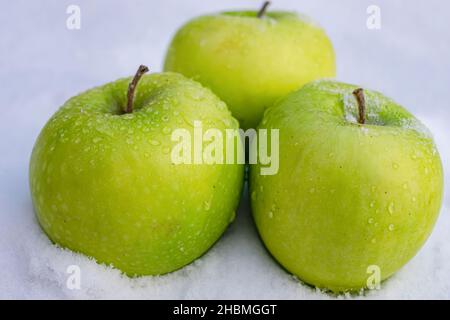 Drei reife und saftige grüne Äpfel, die mit Wassertropfen bedeckt sind, liegen auf dem geschmolzenen Schnee Stockfoto