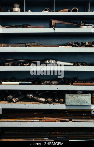 Regal mit Regalen in der Drehbank im Werk. Auf Regalen befinden sich Teile und Rohlinge für die Bearbeitung mit Metall. Industrieller Hintergrund. Länge Arbeitsplatz Wender. Stockfoto