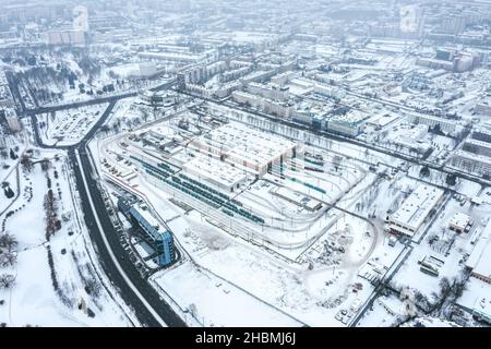 Luftpanorama des Straßenbahndepots im Winter an nebligen Tagen. Urbanes Industriegebiet mit schneebedeckten Gebäuden nach Schneefall. Stockfoto