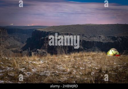 Grünes Zelt am Rand der Klippe mit dem Hintergrund der Schluchten des Ihlara-Tals in der Nacht. Aktivitäten und Trekking in der Türkei. Stockfoto