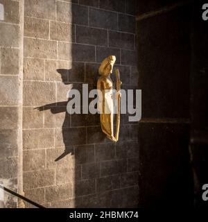 Eine vergoldete Holzskulptur des Pilgers in der Kathedrale von Le Puy-en-Velay, die einen Schatten auf der Wand dahinter fängt Stockfoto