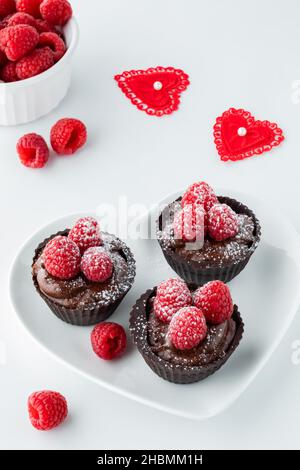 Drei Schokoladen-Himbeer-Becher auf einem herzförmigen Teller zum Valentinstag. Stockfoto