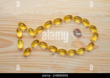 Goldene Fischöl-Kapseln, auf Holzboden, Fisch aus transluziden Kapseln. Stockfoto