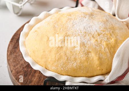 Roher Hefeteig mit Kürbis in weißer Schüssel mit Handtuch auf dem bemehlten Küchentisch bedeckt, Rezeptidee. Konzept Hausbacken Brot, Brötchen oder Cinnabon o Stockfoto