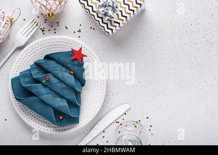 Weihnachtliche Tischaufstellung in weißer Farbe mit schwarzem Besteck, Serviette als Weihnachtsbaum gefaltet, weihnachtliche Silberkugeln, Champagner, Gläser auf weißem Rücken Stockfoto