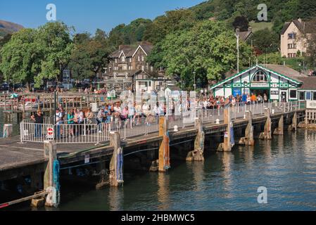 Touristen aus dem Lake District sehen im Sommer Menschen am Ambleside Pier, die sich für ein Ausflugsboot anstehen, um sie auf eine Kreuzfahrt auf dem Lake Windermere, Cumbria, Großbritannien, zu bringen Stockfoto
