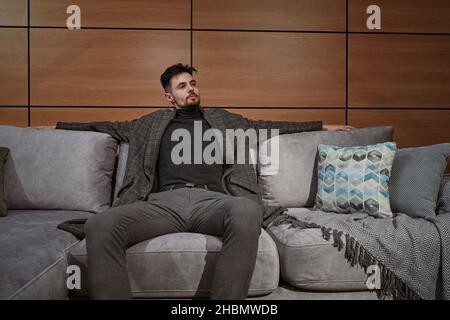 Nachdenklicher junger Mann, der sich im Möbelgeschäft für ein neues Sofa entschieden hat Stockfoto