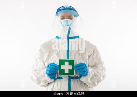 Krankenschwester in PSA und Latexhandschuhen mit einem grünen Schild mit einem Kreuzsymbol für medizinisches Personal. Coronavirus, Pandemie und Gesundheitskonzept. Stockfoto