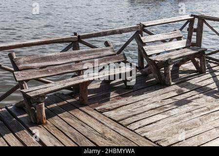 An einem sonnigen Tag stehen alte Holzbänke am Ende eines Piers Stockfoto