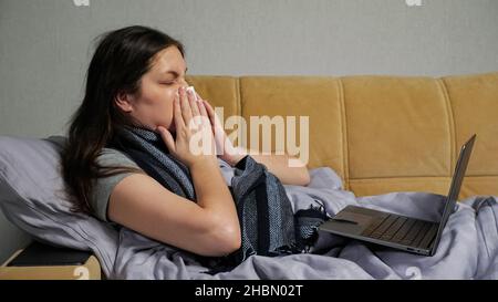 Kranke Frau mit laufender Nase arbeitet entfernt mit Laptop Stockfoto