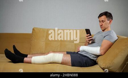 Mann mit verletzten Knie und gebrochenem Arm rollt durch das Telefon Stockfoto