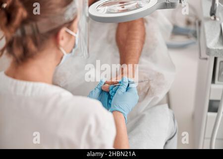 Spezialist entfernt Nagelhaut aus dem Zehennagel des Menschen Client mit Metallsonde im Salon Stockfoto