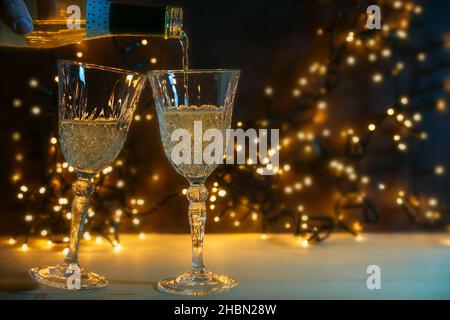 Zwei Gläser werden mit Champagner für einen Neujahrsfest-Toast gegossen, goldene Bokeh-Lichter im dunklen Hintergrund, Kopierraum, ausgewählter Fokus, enge Tiefe Stockfoto