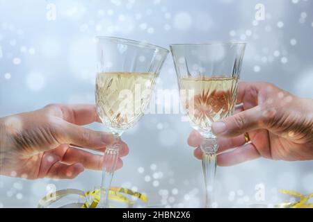 Zwei Hände toasten mit Sektgläsern auf einer Neujahrs- oder Weihnachtsfeier, heller schneebedeckter Hintergrund, ausgewählter Fokus, enge Schärfentiefe Stockfoto