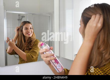 Attraktive junge Frau, die trockenes Shampoo auf ihr Haar anwendet. Schnelle und einfache Möglichkeit, das Haar sauber zu halten mit Trockenshampoo. Stockfoto