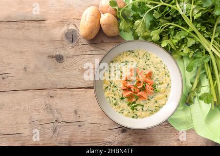 Aus Petersilie gekochte Gemüsesuppe und Kartoffeln serviert mit Lachsstreifen auf einem rustikalen Holztisch, Kopierraum, Blick aus der Höhe von oben Stockfoto
