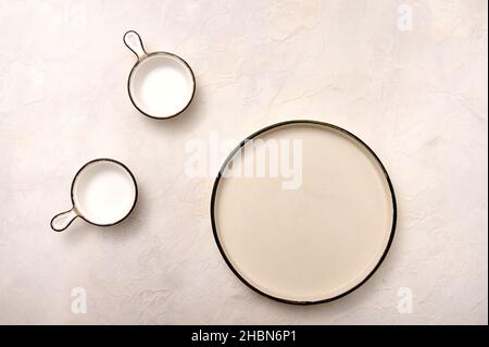 Konzept Set aus leerem Teller und Kochtöpfen mit schwarzem Rand auf hellem Marmorhintergrund. Flach liegend. Speicherplatz kopieren Stockfoto
