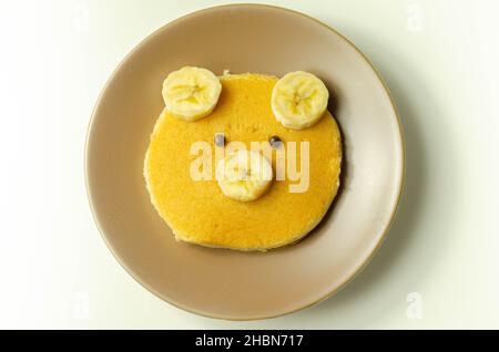 Kreative Mahlzeit für ein Kind, Pfannkuchen mit Banane und Schokolade in einem Gesicht kleine Bärenform, lustige Lebensmittel Stockfoto