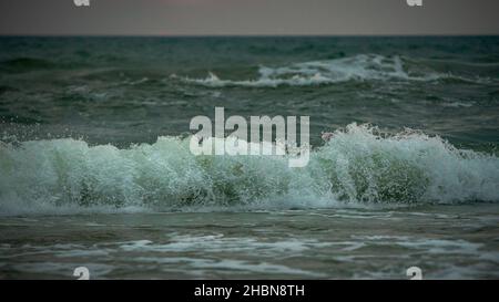 Wellen im Meer mit weißem Schaum am Abend bei Sonnenuntergang, aber die Sonne ist hinter den Wolken versteckt Stockfoto