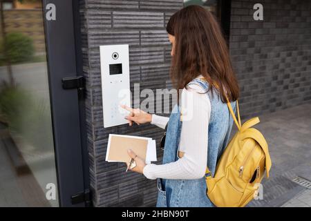 Türzugangskontrolle - eine junge Studentin, die eine Post in den Händen hält, gibt den Code ein, um die Tür zu öffnen. Türcode Stockfoto