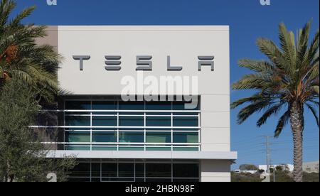 Carlsbad, CA USA - 12. Dezember 2021: Tesla-Schild auf einem kalifornischen Händlergebäude, eingerahmt von Palmen und blauem Himmel Stockfoto