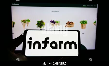 Person, die Mobiltelefon mit Logo der deutschen Firma infarm - Indoor Urban Farming GmbH auf dem Bildschirm vor der Webseite hält. Konzentrieren Sie sich auf die Telefonanzeige. Stockfoto