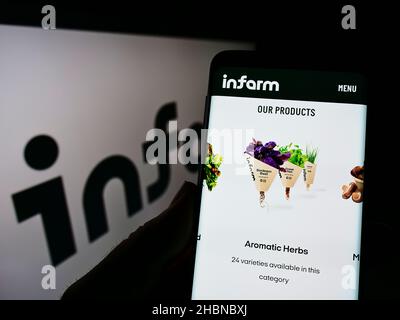 Person mit Mobiltelefon auf der Webseite der deutschen Firma infarm - Indoor Urban Farming GmbH auf dem Bildschirm mit Logo. Konzentrieren Sie sich auf die Mitte des Telefondisplays. Stockfoto