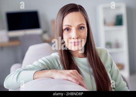 Foto von dremy Millennial Brünette Dame sitzen auf Sofa tragen blaues Hemd zu Hause allein Stockfoto