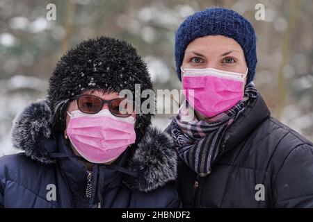 Ältere ältere Frau mit ihrer jüngeren Tochter in warmer Winterkleidung, beide tragen eine rosa Einweg-Virus-Gesichtsmaske Stockfoto