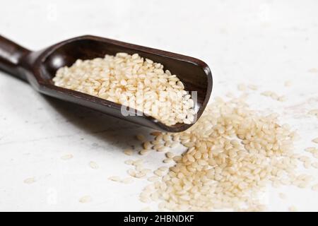Weiß Sesam - gehören insbesondere Indicum - Samen in kleinen Holzlöffel auf weißem Stein wie Board Stockfoto