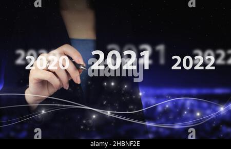 Konzept Start Neujahr 2022. Hand hält digitalen Grafikstift und Zeichnung digitalen Hologramm 2021sign auf Stadt dunkel verschwommen Hintergrund. Erfolg im neuen Jahr Stockfoto