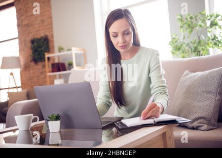 Foto von nachdenklich glänzend reifen Dame tragen teal Pullover lächelnd sitzend Couch Schreiben Copybook moderne Gadget drinnen Hauszimmer Stockfoto