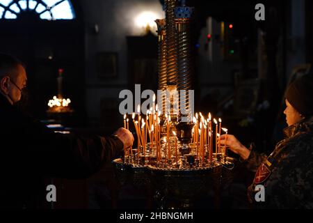 Swjatohirsk, Ukraine. 19th Dez 2021. Eine ukrainische Militärangehörende und ein Zivilist haben in der Mariä Himmelfahrt-Kathedrale brennende Kerzen aufgestellt.die Heilige Mariä Himmelfahrt Sviatohirsk Lavra ist ein wichtiges geistliches Zentrum der Ostukraine. Das orthodoxe Kloster befindet sich am rechten hohen Kreideufer des Flusses Siverskyi Donez (auf den sogenannten Heiligen Bergen) in der Stadt Swjatohirsk im Norden der Region Donezk. (Foto von Andriy Andriyenko/SOPA Images/Sipa USA) Quelle: SIPA USA/Alamy Live News Stockfoto